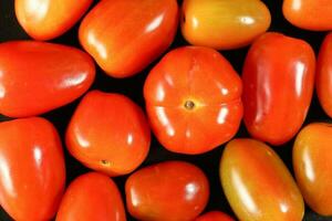 färsk mogen små skinande röd tomat på svart bakgrund foto
