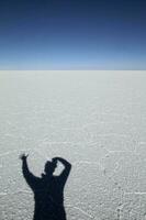 skugga av en man tar en Foto av de omfattande vit yta av de salar de uyuni i bolivia