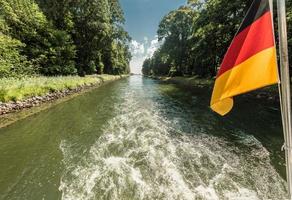 drivaxel av en båt på en kanalpassage med viftande tysklands flagga foto