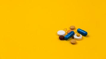 flerfärgade tabletter och piller kapslar från glasflaskan på gul bakgrund foto