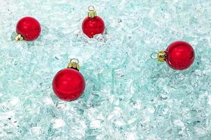 röda glasbollar med guldhängare ligger på glittrande glasskärmar