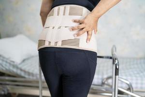 asiatisk dampatient som bär ryggvärkstödbälte för ortopedisk ländrygg med rullator foto