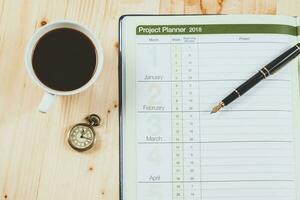 personlig projekt planerare med fontän penna och varm kaffe på trä tabell. foto