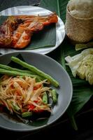 thai mat maträtt både i thailand och Asien, papaya sallad eller som vi ring upp den somtum är kompletteras med grillad kyckling och klibbig ris med färsk röror. eras på de svart trä- tabell. foto