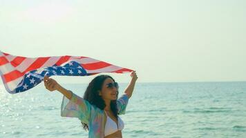 ung kvinnor håll amerikan flaggor på de strand och de hav på deras sommar semester och de leende och njut av deras semester. foto