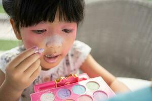 förtjusande liten barn asiatisk flicka målarfärger henne mun med rosa barn huvuden och utseende i de spegel. en barn spelar på Hem i en leksak skönhet salong. öka inlärning utveckling för förskolebarn. foto