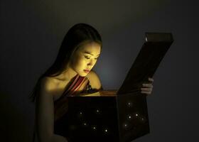 asiatisk kvinna öppning mystiker bok låda magisk ljus mörk bakgrund foto