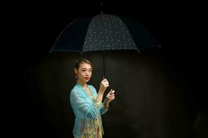 asiatisk kvinna i dragkraftig kebaya bärande paraply på svart bakgrund foto