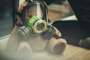 barn med teddy Björn bär gas mask ser ut de fönster. foto