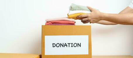 donation, välgörenhet, volontär, ger och leverans begrepp. hand innehav kläder in i donation låda på Hem eller kontor för Stöd och hjälp fattig, flykting och hemlös människor. kopia Plats för text foto