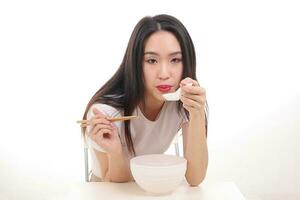 skön ung söder öst asiatisk kvinna innehav kinesisk tömma matpinne soppa sked skål redskap låtsas verkande Framställ ser äta smak utfodra erbjudande tillfredsställelse smaskigt vit bakgrund Lycklig foto