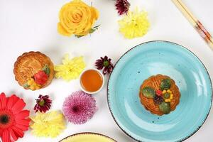 färgrik blomma dekorerad måne kaka kinesisk mitten höst festival te i små vit tekopp ätpinnar plattor skål blå gul violett krysantemum mamma röd daisy blomma på vit bakgrund foto