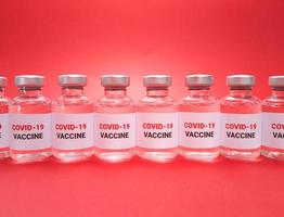 många flaskor med covid 19-vaccin i rad på röd bakgrund foto