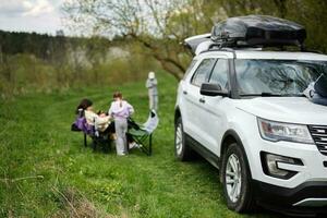 sUV bil med tak kuggstång låda mot familj på picknick. foto