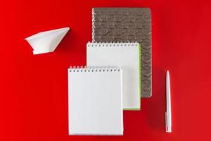 kontorsmateriel - anteckningsböcker och pennor på en röd bakgrund foto