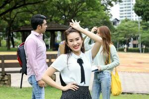 ung asiatisk malaysiska kinesisk man kvinna utomhus- parkera promenad stå studie prata diskutera punkt bärbar dator fil bok ryggsäck kvinna se framåt- ok finger tecken foto