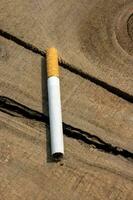 cigarett på en trä- yta stänga upp skott. nikotin missbruk begrepp med en full cigarett. ohälsosam rökning vana och cigarr missbruk begrepp. cigarett stänga upp på en bruten trä- yta. foto