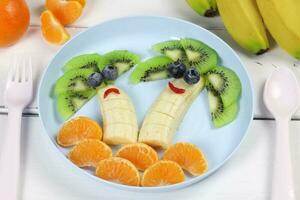 kreativ mat för en barn, kiwi, mandariner och banan. frukt handflatorna. rolig mat på färgad redskap. frukt för en barn. se från ovan. foto