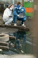 nödsituation förorening fabrik begrepp. ingenjörer bär mekaniker jumpsuits och ppe och gas masker inspektera olja på de fabrik golv. foto