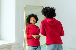 kärlek själv. skön ung leende afrikansk amerikan kvinna dans njuter henne spegel reflexion. svart lady ser på spegel ser självsäker och Lycklig. själv kärlek begrepp. foto