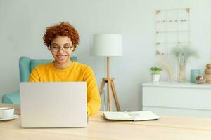 afrikansk amerikan flicka använder sig av bärbar dator på Hem kontor ser på skärm skriver chattar läsning skrivning e-post. ung kvinna har virtuell möte uppkopplad chatt video ring upp konferens arbete inlärning från Hem foto