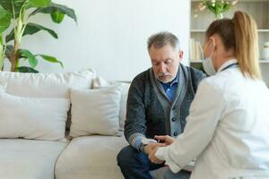 kvinna läkare senior man tar hans blod tryck i läkare kontor eller på Hem. gammal man patient och läkare ha samråd i sjukhus rum. medicin sjukvård medicinsk kolla upp. besök till läkare. foto