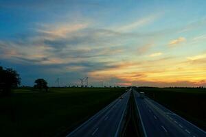 motorväg med bil trafik och väderkvarn turbiner på solnedgång foto