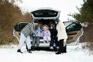 familj med barn sitta på bil sUV med öppen trunk stå i vinter- skog. foto