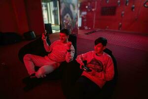far och son spela gamepad video spel trösta i röd gaming rum. pappa och unge spelare. foto