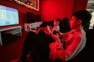 två Pojkar spelare spela fotboll gamepad video spel trösta i röd gaming rum. foto
