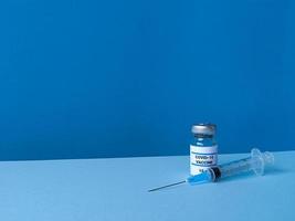 medicinsk flaska med covid 19-vaccin och spruta på blå bakgrund med lutande trendig skyline och kopieringsutrymme foto
