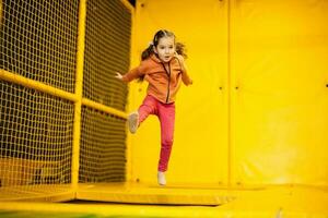 liten flicka unge Hoppar på trampolin på gul lekplats parkera. barn i rörelse under aktiva underhållning. foto