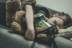 sovande flicka med teddy Björn i gas mask. foto