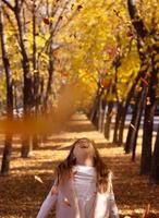 vacker liten flicka som kastar fallna löv som leker i parken med höstens naturbakgrund foto