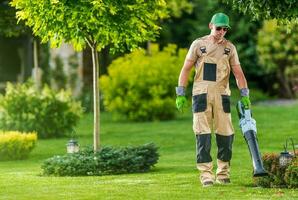 trädgårdsmästare blåser löv av de gräsmatta foto