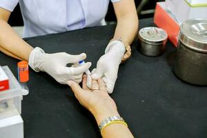 händer av sjuksköterska ha på sig en sudd vit medicinsk handske innehav blod lansett nål penna hugg på mänsklig ringa finger till kolla upp glukos i blod på medicinsk klinik. foto