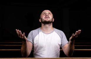 en kristen man i vit skjorta sitter med händerna uppe och ber med ödmjukt hjärta i kyrkan foto
