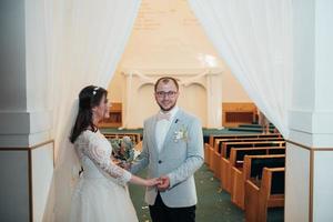 unga bruden och brudgummen på deras bröllopsdag i en kyrklig byggnad foto