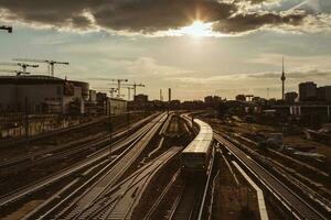 tåg lämnar de berlin tåg station med de bakgrundsbelysning av de gyllene solnedgång, med bangård runt om och de silhuett av de stad och kranar i de bakgrund foto