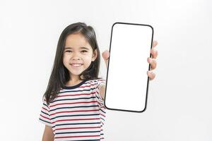 asiatisk liten flicka innehav smartphone attrapp av tom skärm och leende på vit bakgrund. foto