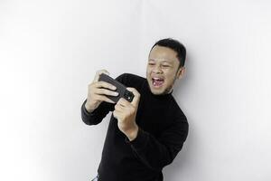ung asiatisk man i tillfällig ha på sig är spelar spel med mobil telefon med en vit bakgrund isolerat. foto
