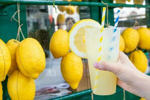 kaukasisk hand med frisk färsk lemonad under sommaren - citron bakgrund foto