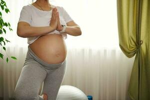 graviditet yoga. närbild förväntans mamma, gravid kvinna med naken mage, Träning träd placera med bön händer på Hem foto