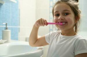 närbild härlig barn flicka pensling tänder, leende med skön leende ser på kamera. dental hälsa. oral hygien foto