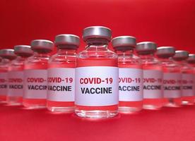många flaskor med covid 19-vaccin på röd bakgrund