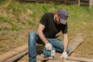 ett vuxen man är engagerad i snickeri arbete på en hus konstruktion webbplats - en trä- staket och terrass styrelser foto