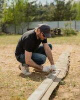man bygger sektioner av staket runt om hans gård ut av plankor - sommar Hem sysslor i de bakgård foto