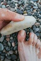 man slipning hans Miniatyr med en sten - bruten, ovårdad nagel - peeling och pedikyr på de strand foto