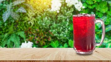 färsk roselle juice ljuv vatten och iced i glas på trä- tabell med natur bakgrund, sommar hälsa drycker med is, röd juice med is kuber i glas foto