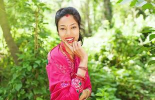ung skön nepalesiska kvinna bär saree stående i en naturlig bakgrund av skog innehav henne händer förbi henne ansikte foto